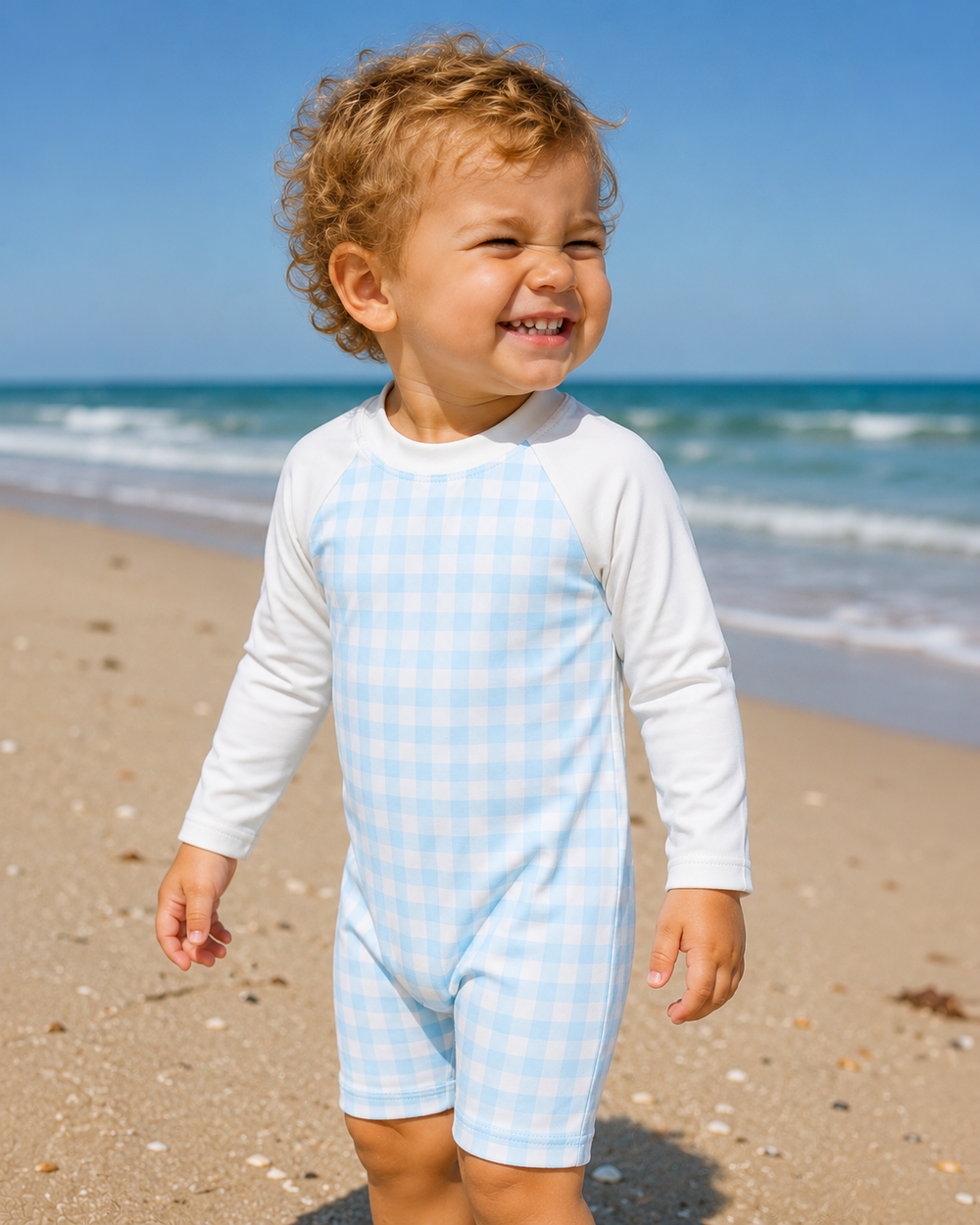 Child wearing a light blue and white checkered outfit on a beach