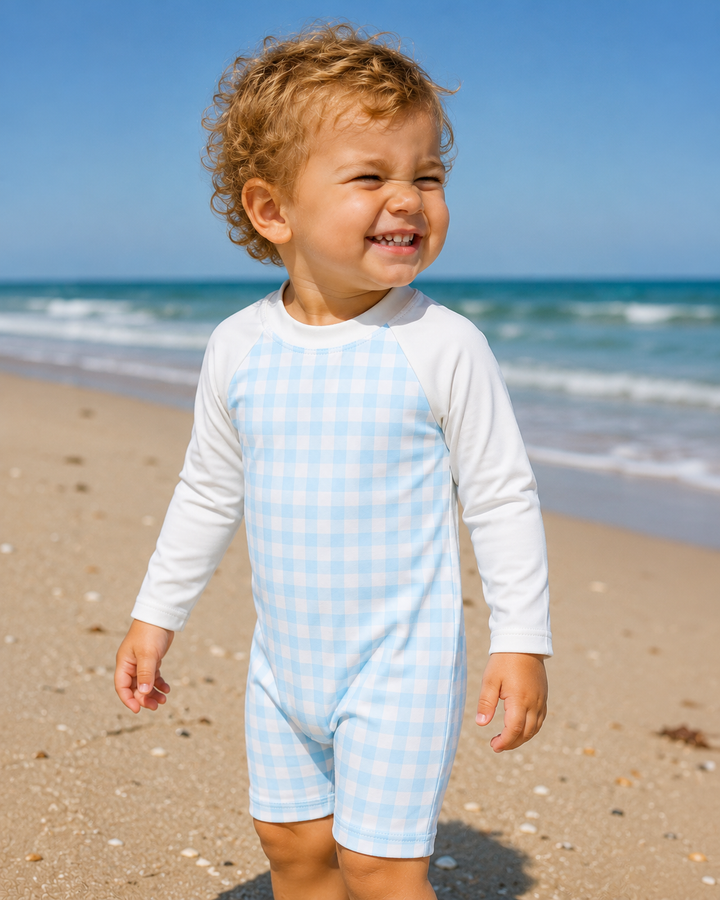 Child wearing a light blue and white checkered outfit on a beach