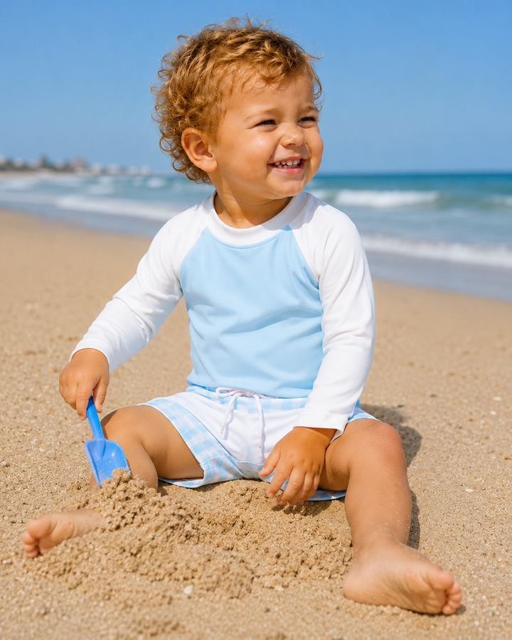 Child playing in the sand on a beach with a blue sky.