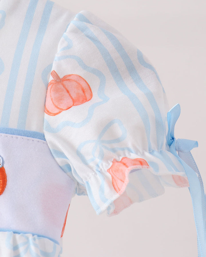 Close-up of a baby clothing garment featuring light blue and white vertical stripes, a white puff sleeve with a peach-orange pumpkin print, and a light blue ribbon tie.