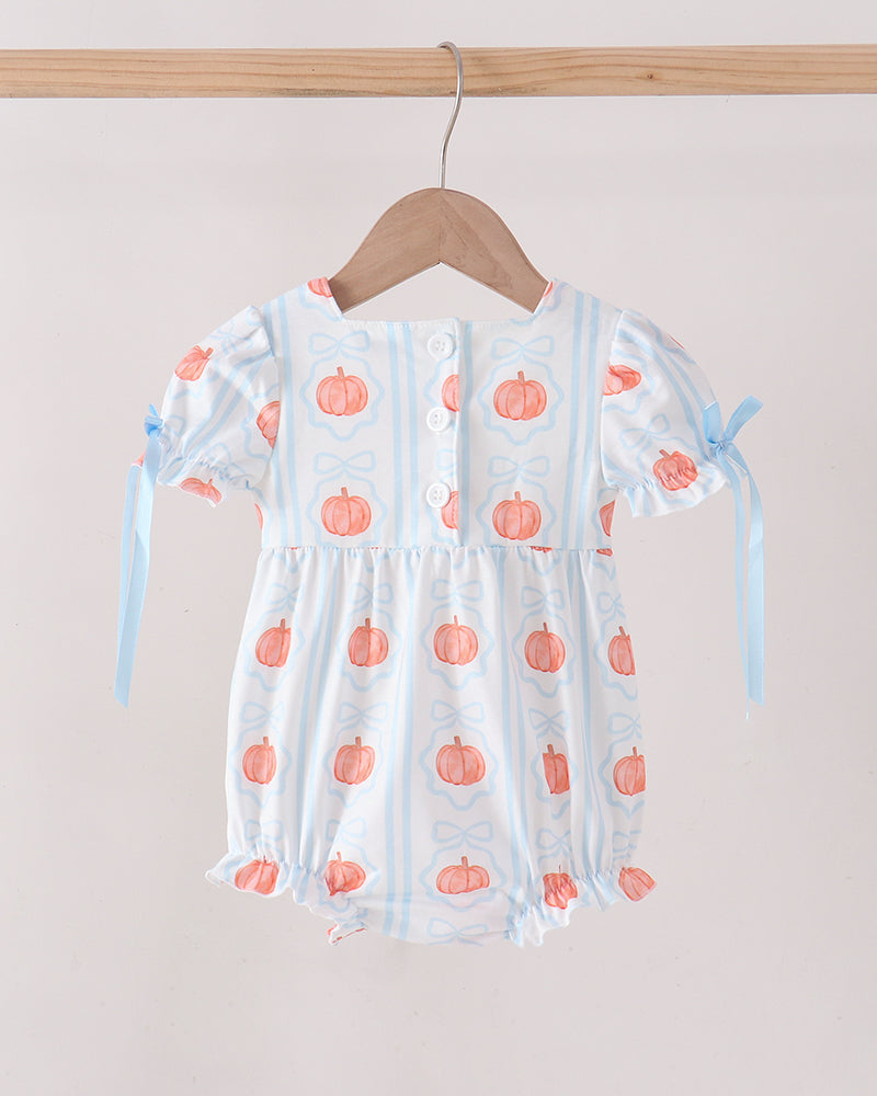 A baby romper with a white base, light blue vertical stripes, and orange pumpkin prints, hanging on a wooden hanger from a wooden rod against a light beige wall.