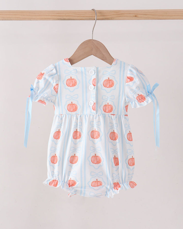 A baby romper with a white base, light blue vertical stripes, and orange pumpkin prints, hanging on a wooden hanger from a wooden rod against a light beige wall.