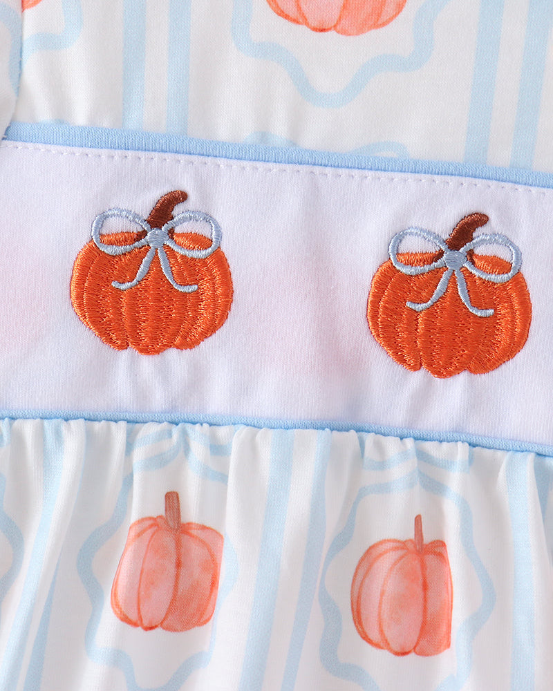 Close-up of a white dress with light blue vertical stripes, orange pumpkin prints, and a light blue band featuring two embroidered orange pumpkins with gray bows.