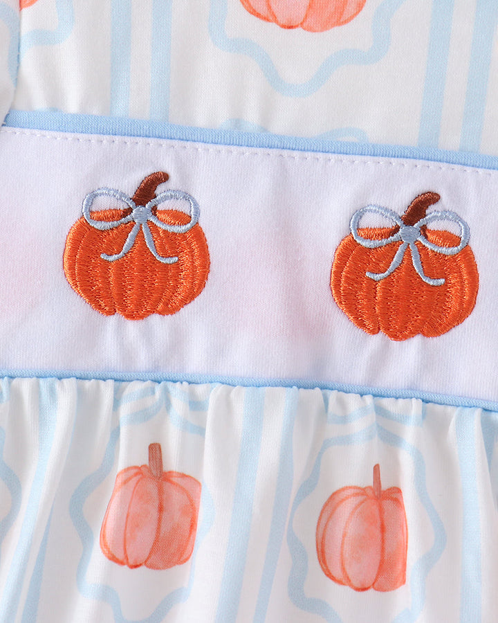Close-up of a white dress with light blue vertical stripes, orange pumpkin prints, and a light blue band featuring two embroidered orange pumpkins with gray bows.