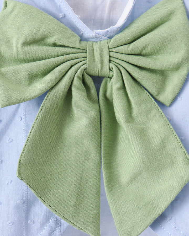 A light sage green fabric bow accessory attached to a light blue textured dress, shown in a close-up shot.