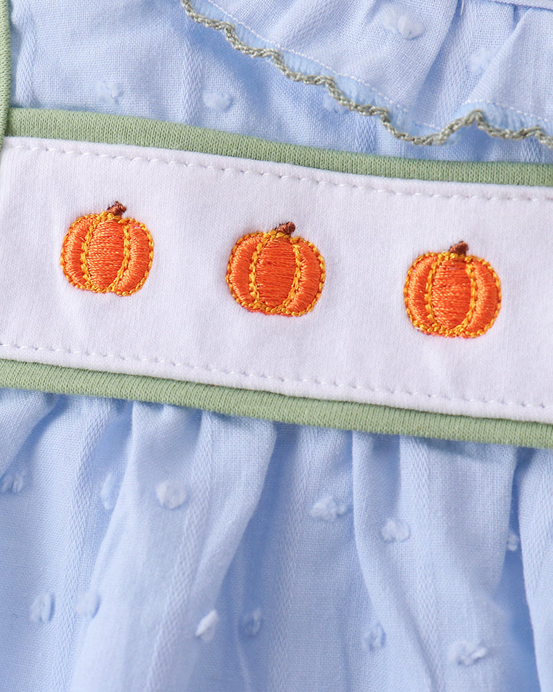 Close-up of a light blue baby dress featuring a white smocked band with three orange pumpkin embroidery motifs and a light green trim.
