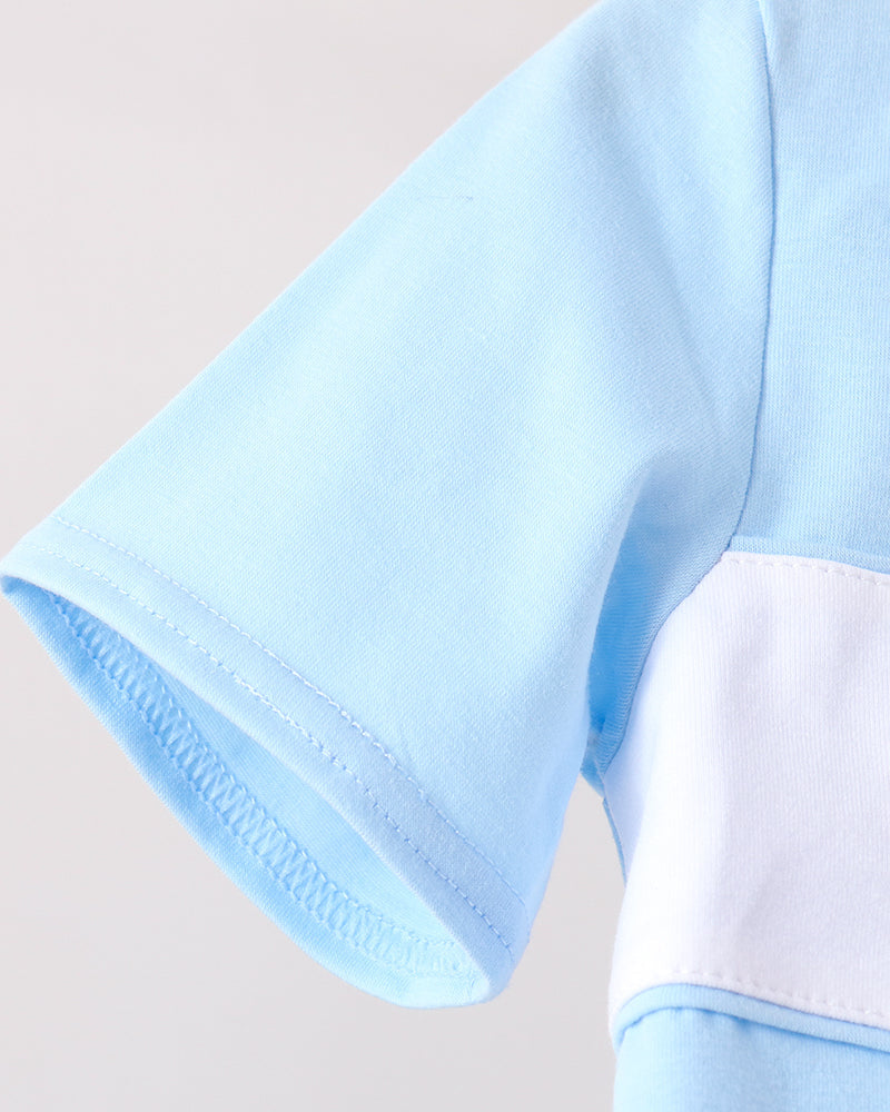 Close-up of a light blue short-sleeve garment with a contrasting white panel on the upper arm, showing the fabric texture and clean stitching.