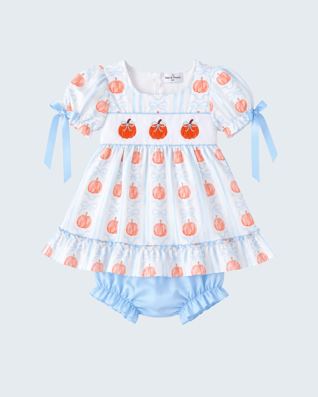 A baby girl's two-piece romper and bloomers set. The smocked dress features a white and light blue vertical stripe pattern with orange pumpkin prints, a white smocked yoke with three embroidered pumpkins, light blue ribbon bows on the sleeves, and a ruffled hem.