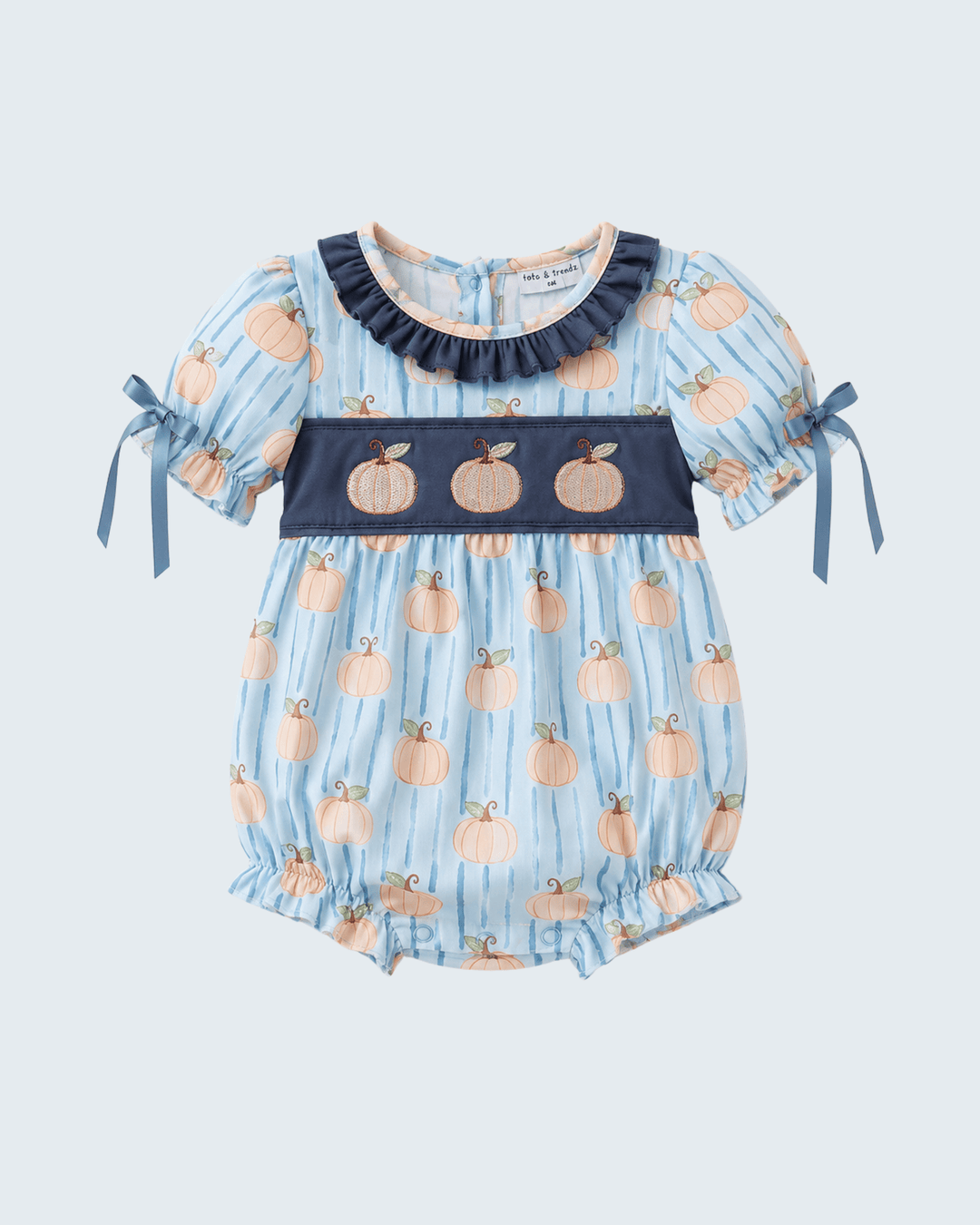 A baby romper in light blue with vertical stripes, featuring a pumpkin print, a navy blue smocked chest panel with three embroidered pumpkins, and navy blue ruffled collar. The short sleeves have navy blue ribbon ties on the sides.