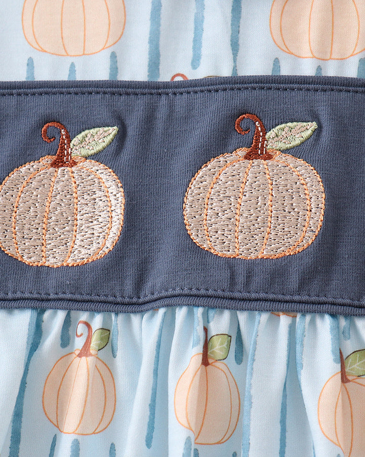 Close-up of a baby dress featuring a navy blue band with embroidered peach pumpkins, above a light blue and white striped fabric with a pumpkin print.