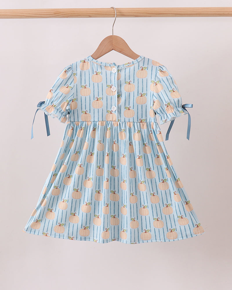 A light blue and white striped short-sleeve dress with a peach-colored fruit print, hanging on a wooden hanger from a wooden clothes rack against a plain beige wall.