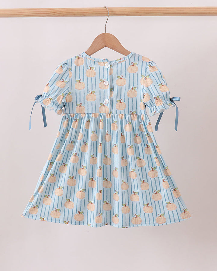 A light blue and white striped short-sleeve dress with a peach-colored fruit print, hanging on a wooden hanger from a wooden clothes rack against a plain beige wall.