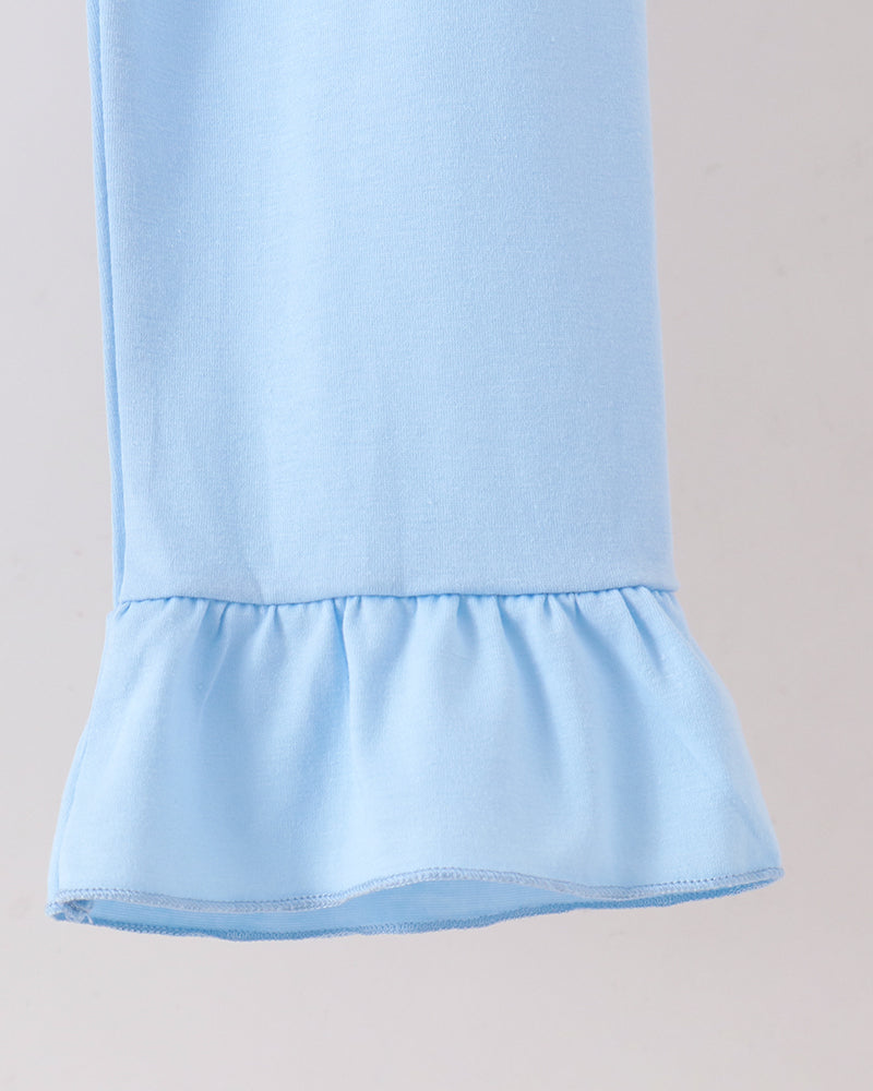 A close-up of a light blue garment, likely a dress or long-sleeve top, featuring a ruffled hem detail against a plain light background.