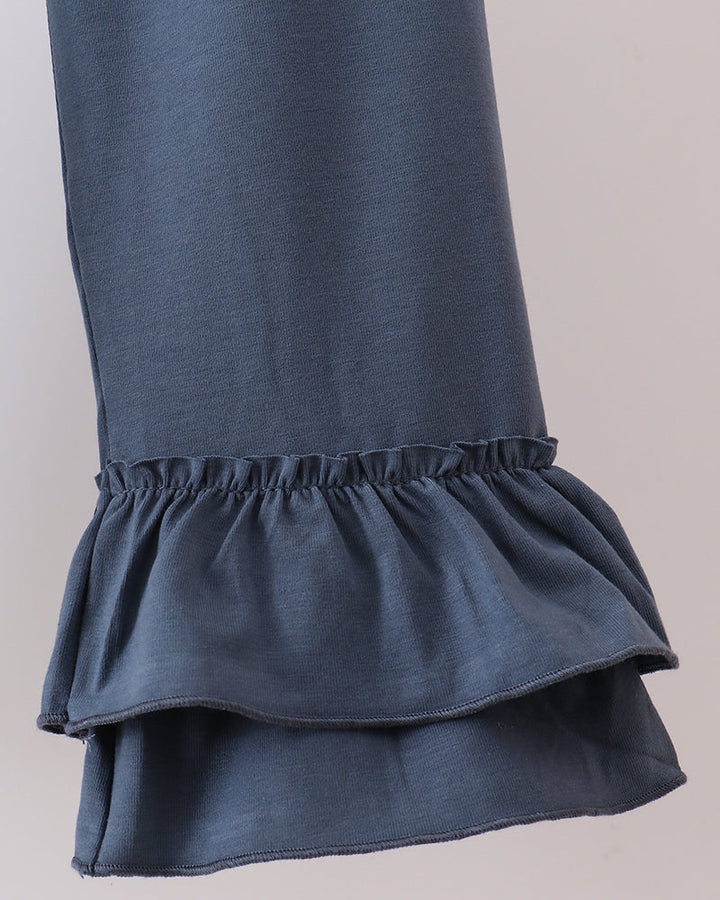 Close-up of a dark slate blue garment featuring a double-layered ruffle hem against a neutral light gray background.