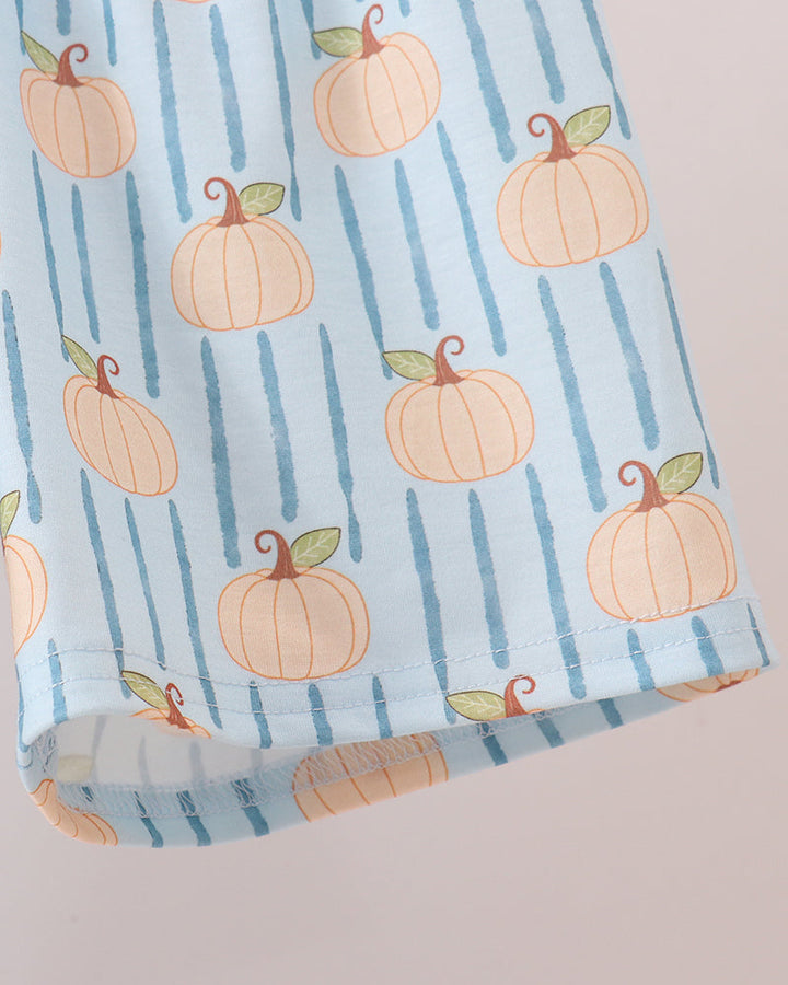 A folded piece of light blue fabric printed with vertical stripes and orange pumpkins with green leaves, set against a solid pale pink background.