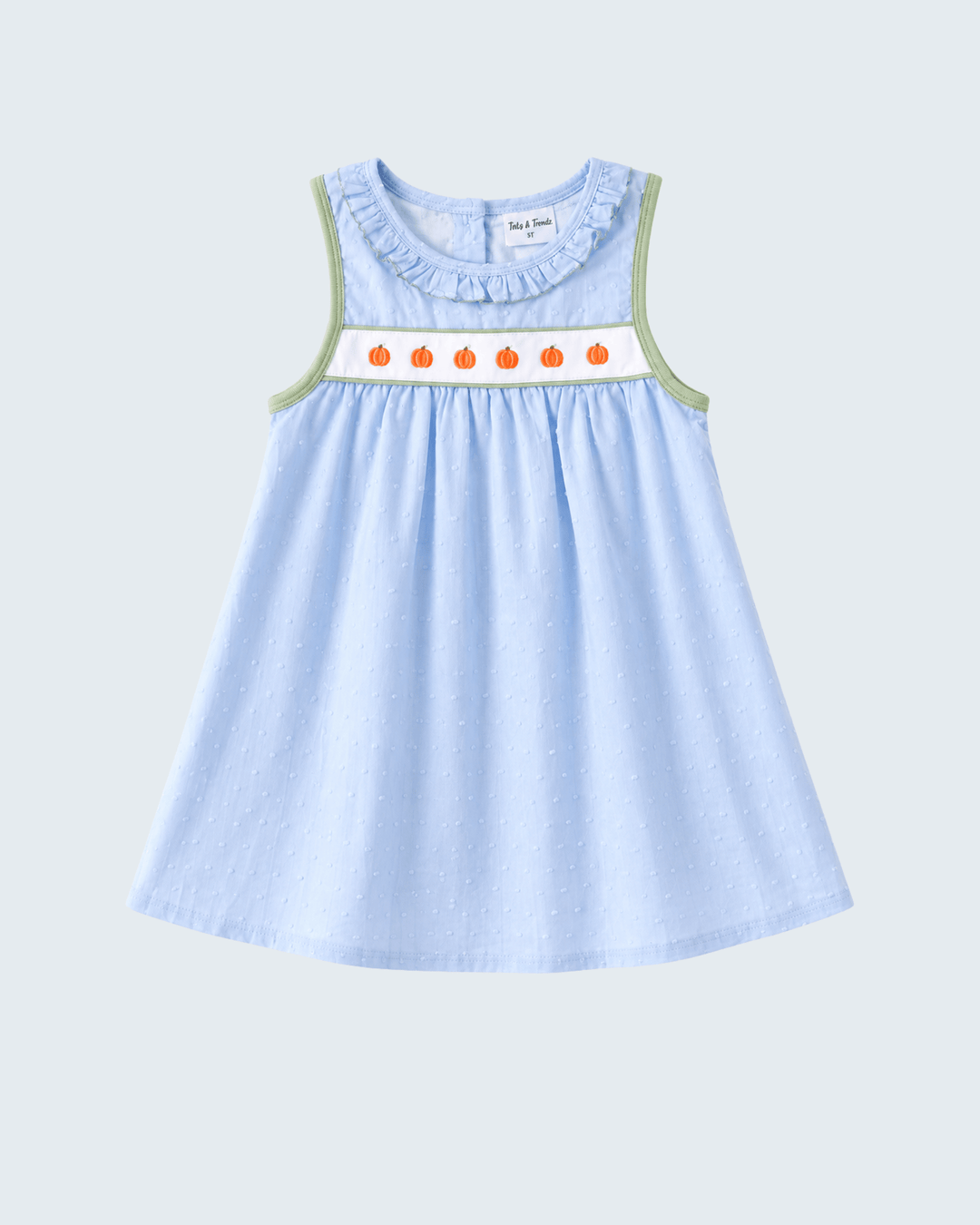 A light blue sleeveless baby dress with a ruffled neckline, featuring a white smocked band with orange pumpkin motifs and sage green trim along the armholes, shown against a light gray background.