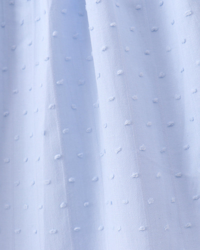A close-up of light blue fabric with a repeating raised dot texture, shown with soft vertical folds.