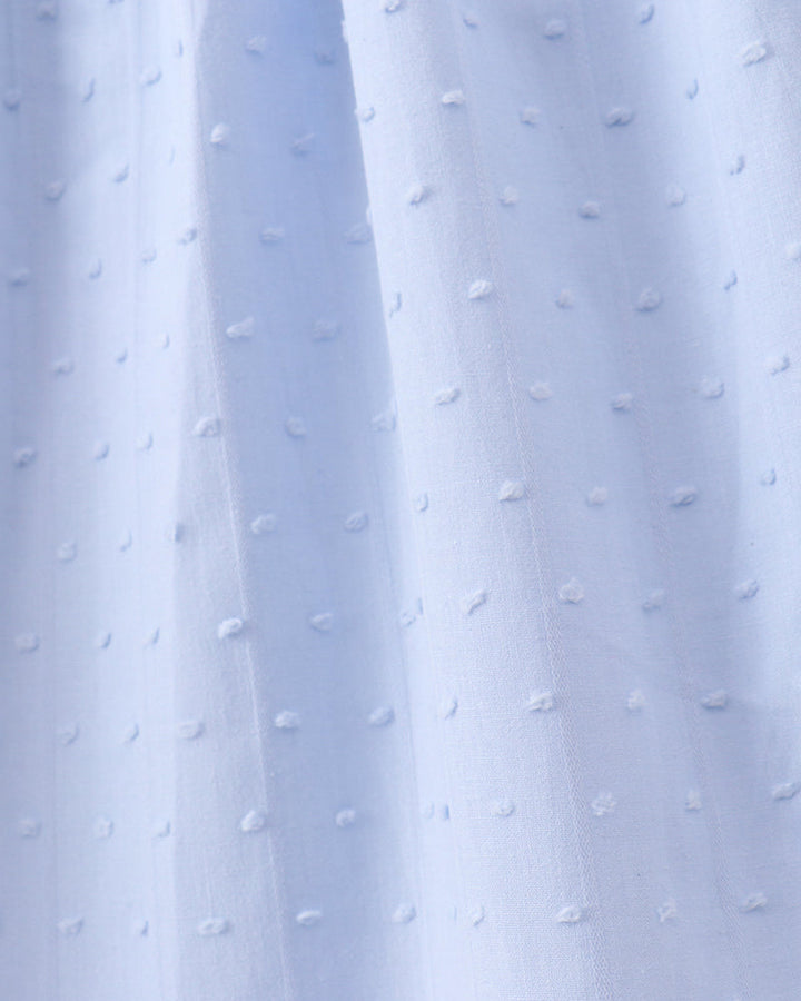A close-up of light blue fabric with a repeating raised dot texture, shown with soft vertical folds.