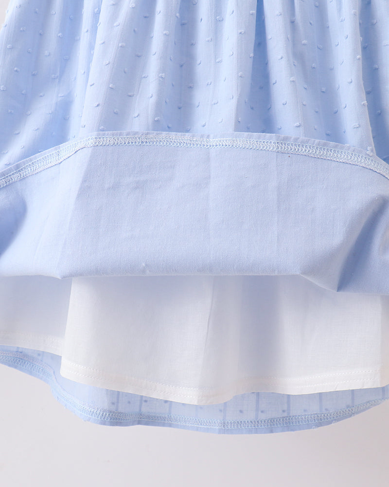 Close-up of a light blue dress or skirt with a textured dotted fabric and a contrasting solid white underlayer or lining, shown against a plain light background.