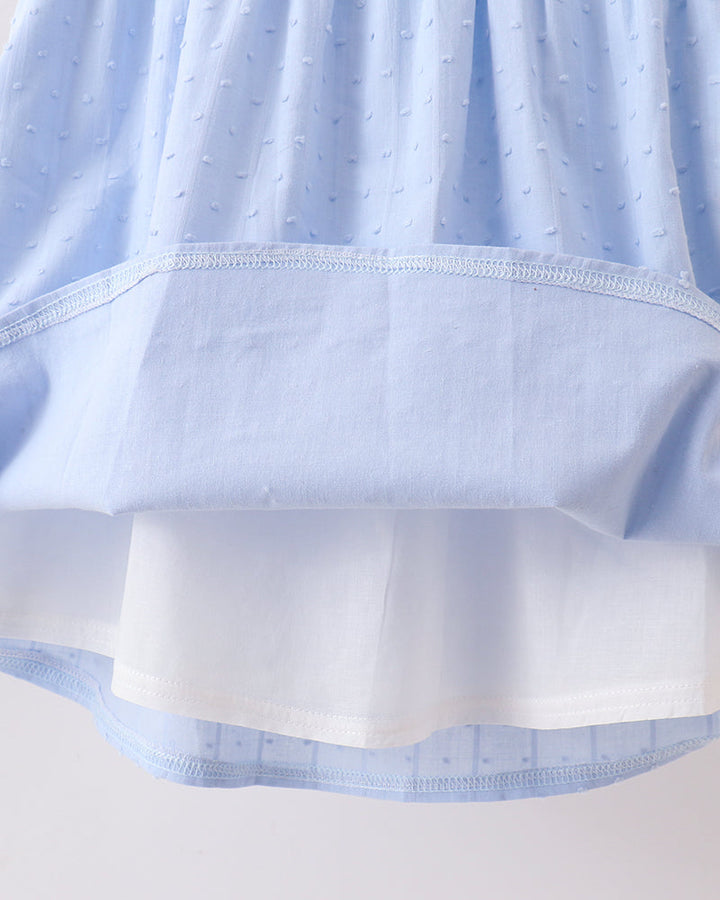 Close-up of a light blue dress or skirt with a textured dotted fabric and a contrasting solid white underlayer or lining, shown against a plain light background.