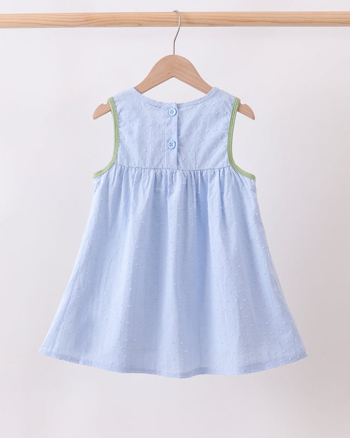 A light blue sleeveless dress with green trim hanging on a wooden hanger against a plain off-white wall.