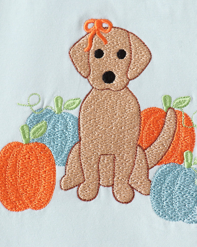 Embroidered autumn dog patch featuring a tan puppy with an orange bow, surrounded by orange and blue pumpkins on a white fabric background.