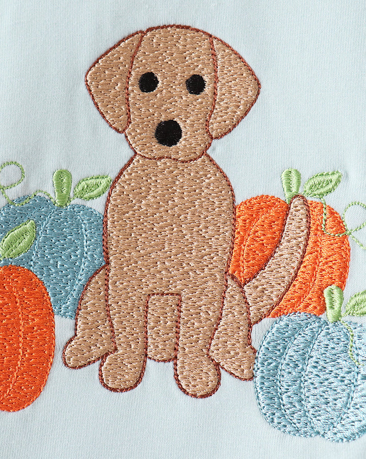 Embroidered autumn dog design featuring a brown dog surrounded by orange and blue pumpkins on a white fabric background.