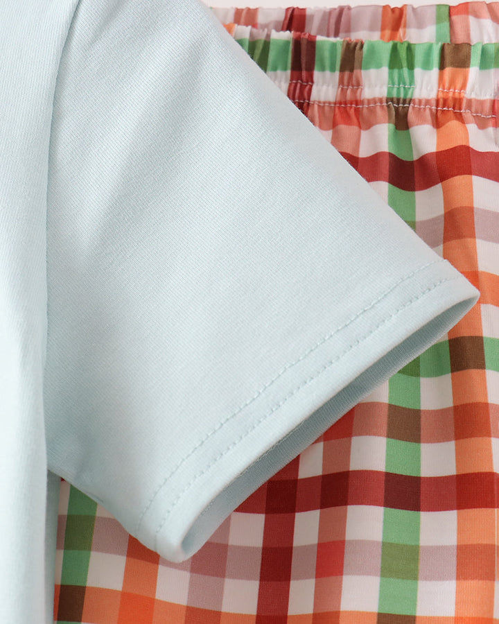 Close-up of a light blue short-sleeve garment laid over a multicolor plaid fabric background.