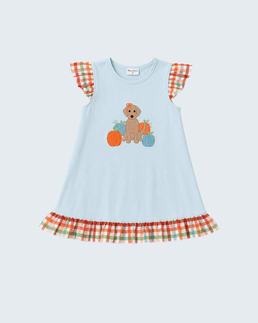 A light blue sleeveless dress with a fall-themed graphic of a puppy and pumpkins on the front, featuring orange, green, and white plaid ruffle details on the shoulders and hem.