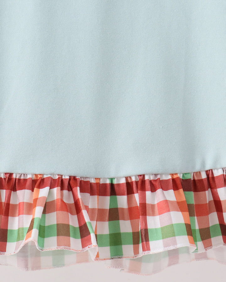 A close-up of a light blue garment with a ruffled hem featuring a red, green, and white plaid pattern.
