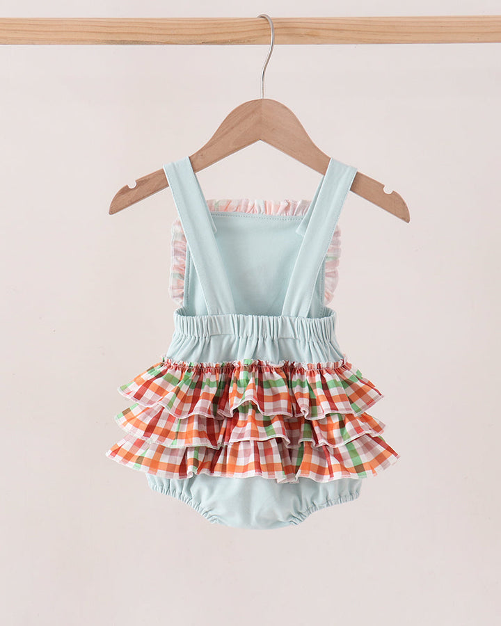 A baby romper with a light blue mint body and a tiered ruffle skirt in a red, green, and white gingham pattern, hanging on a wooden hanger against a light beige background.