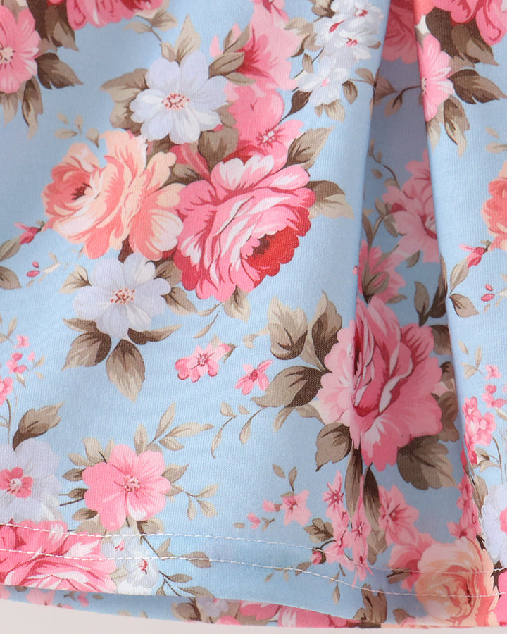 A close-up of a light blue fabric with a floral print featuring pink and white roses with brown leaves.