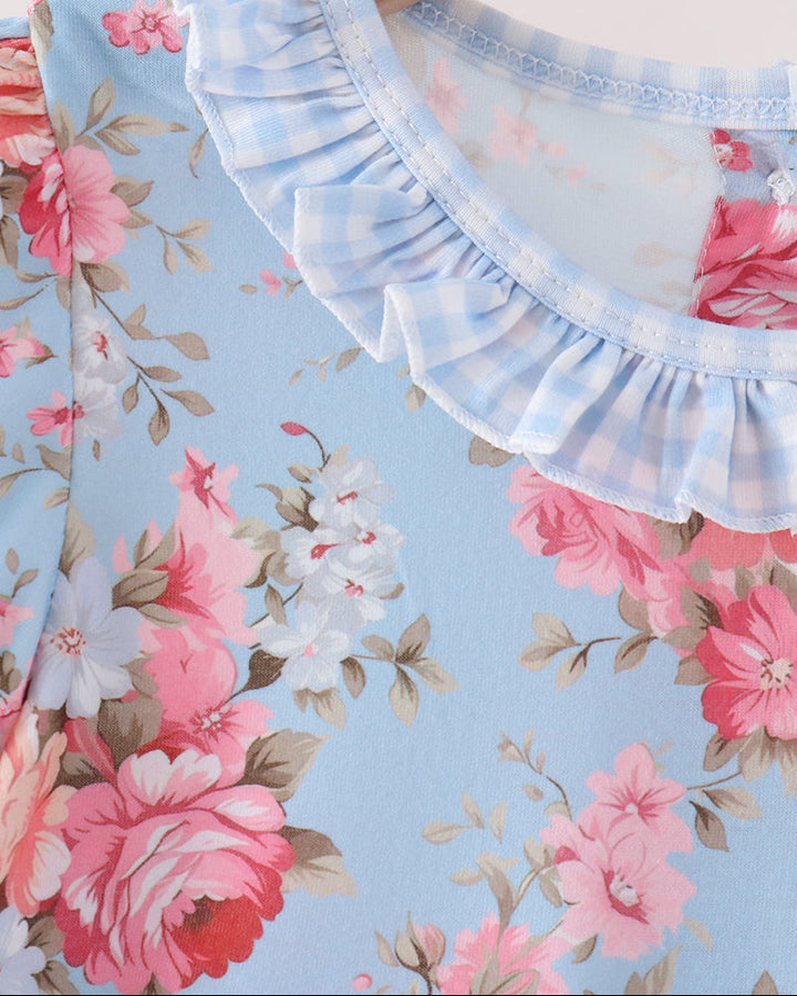 Close-up of a light blue floral top with pink and white flowers, featuring a light blue and white gingham ruffled collar, hanging on a wooden hanger.