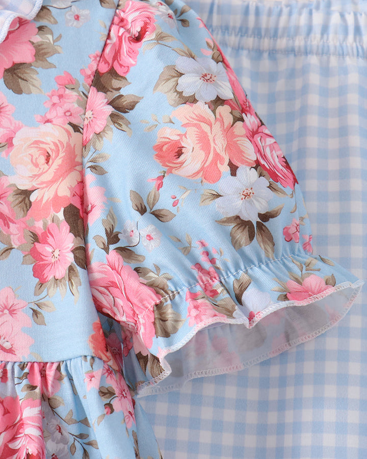 A close-up of a light blue floral dress or romper with pink and white roses, paired with matching light blue and white gingham bottoms.