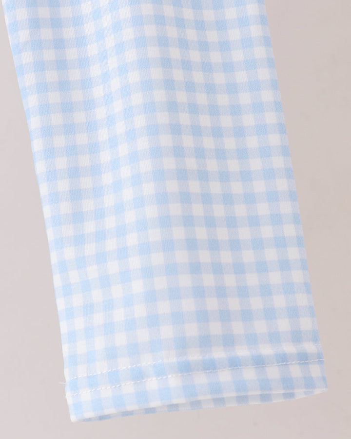 A close-up of a light blue and white gingham fabric, showing the fine checkered pattern and a neat hemmed edge against a plain light background.