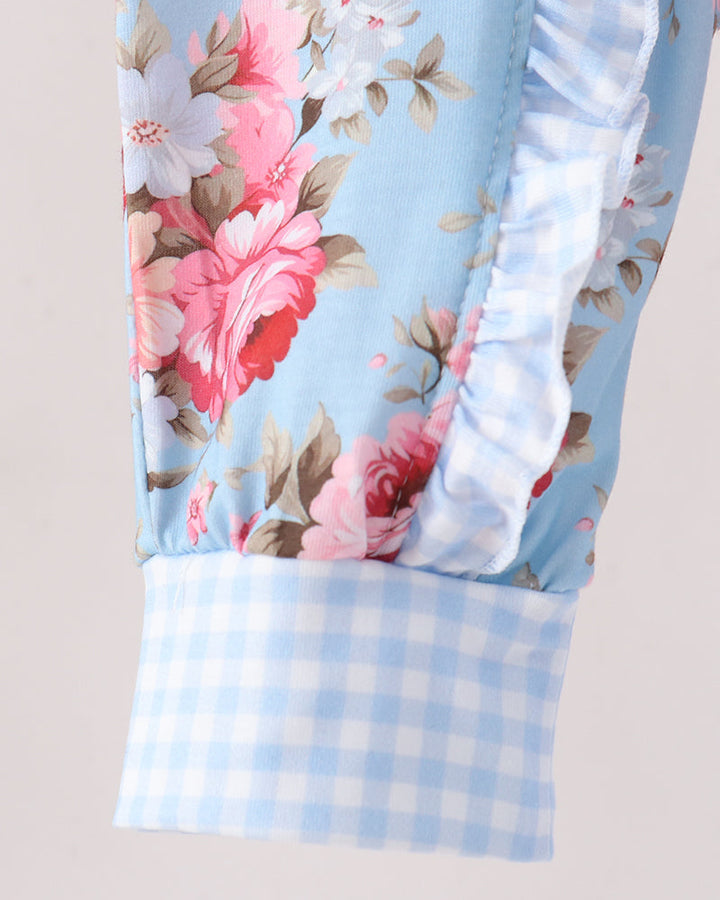 Close-up of a light blue floral fabric garment with pink and white flowers, a ruffled trim, and a light blue and white gingham cuff.