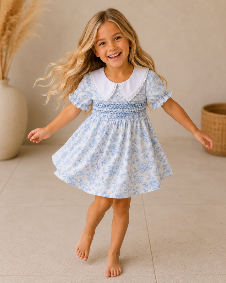 Young girl in a blue floral dress standing on a tiled floor with a neutral background