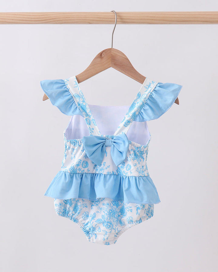 Blue floral swimsuit with ruffles on a wooden hanger against a white background