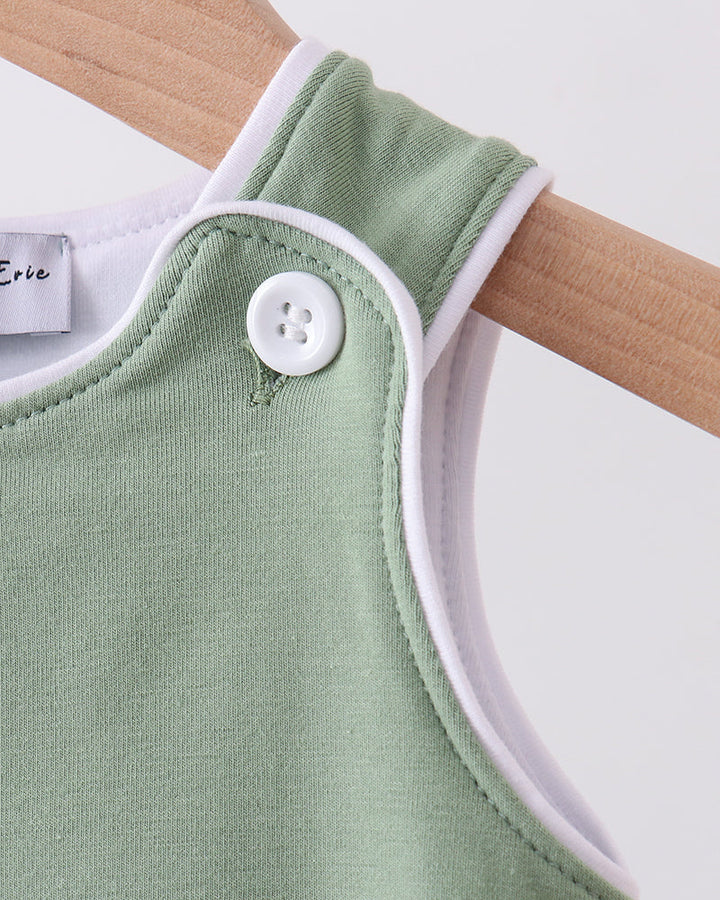 Green baby romper with white trim on a wooden hanger against a white background