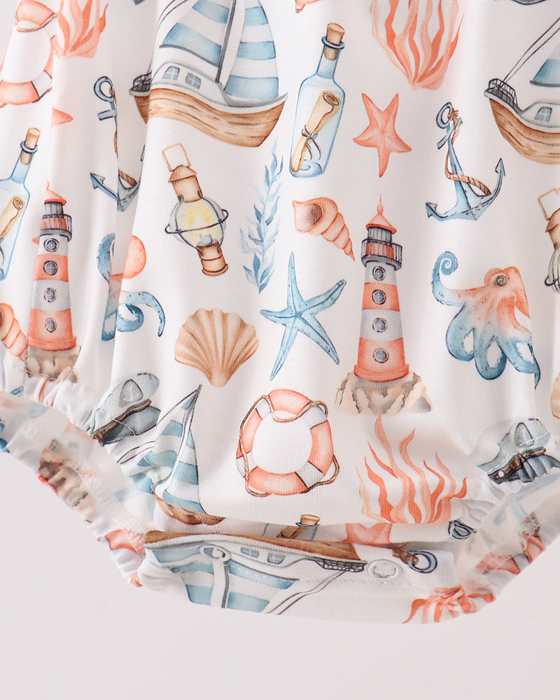 Close-up of a baby romper or diaper cover featuring a nautical-themed print with lighthouses, starfish, seashells, bottles, and sea urchins on an off-white background.