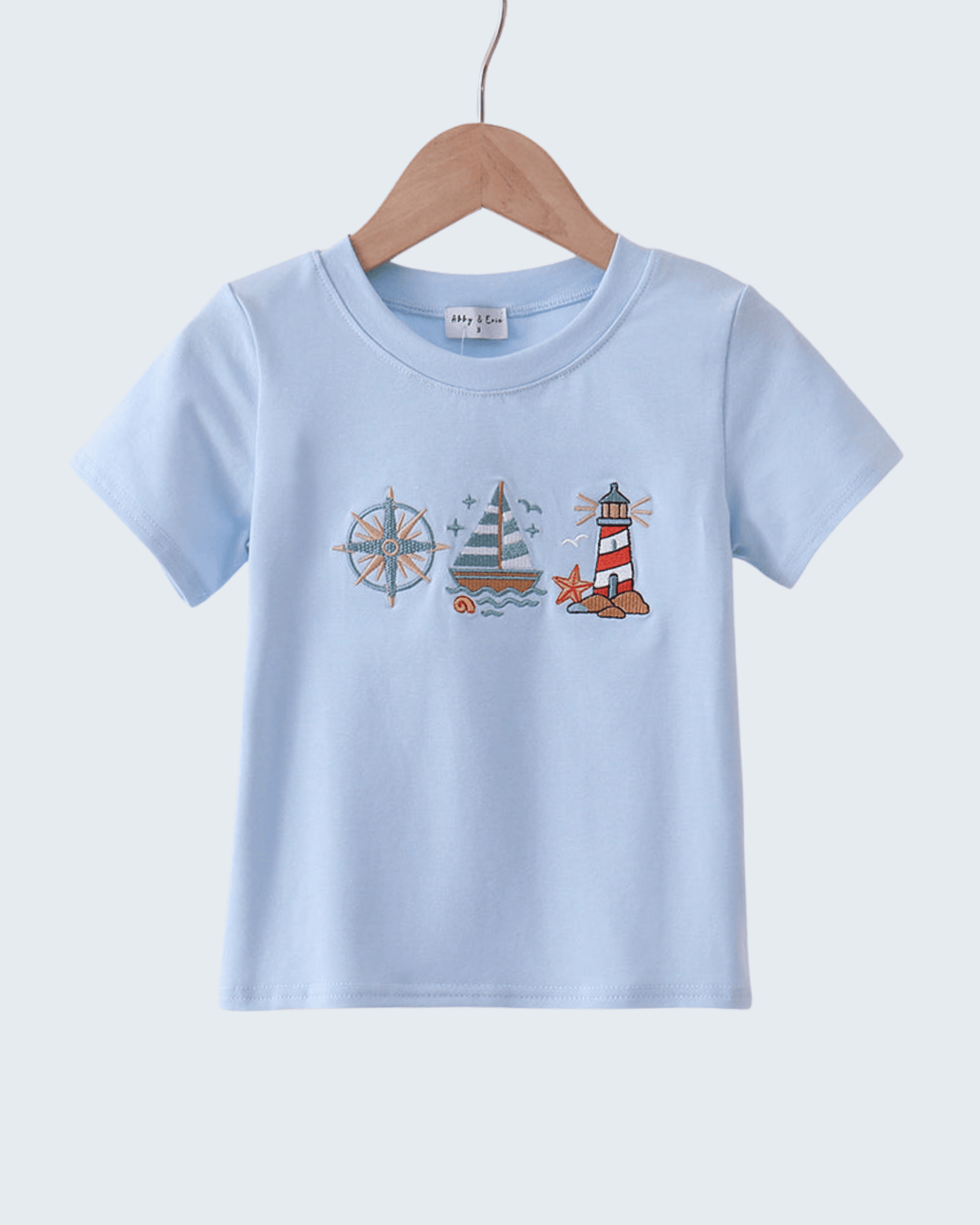 Light blue t-shirt with nautical-themed design on a wooden hanger against a white background