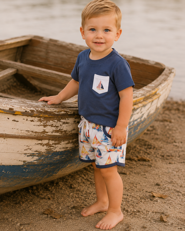Young boy is standing by a wooden boat by the water