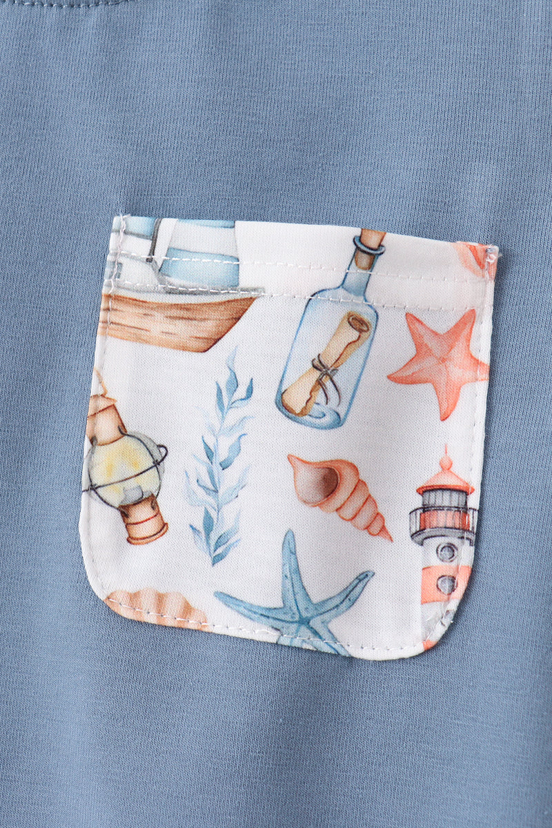 Close-up of a light blue fabric garment featuring a front pocket with a white background and a colorful nautical print of starfish, a bottle with a letter, a lighthouse, a seashell, and a boat.