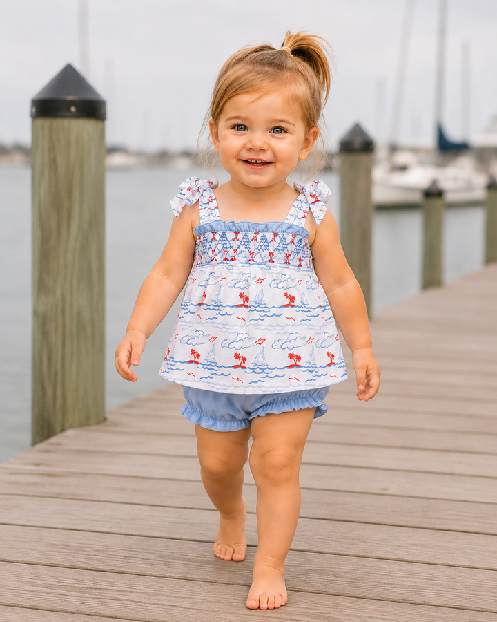 Child in a blue and white dress with flamingo pattern walking on a dock by water.