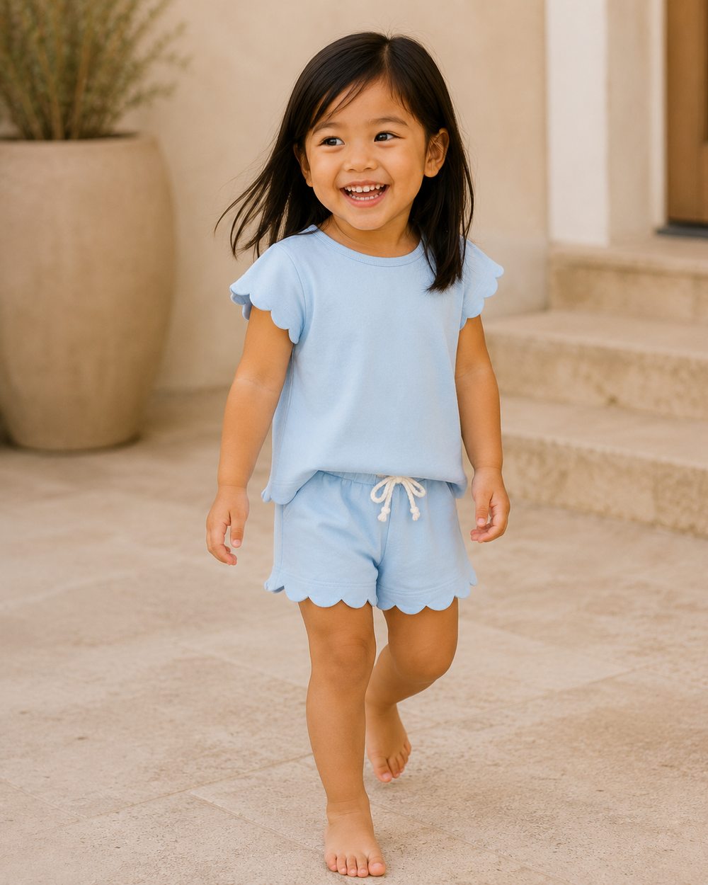 Child wearing a light blue outfit with ruffled sleeves and shorts, standing on a stone path.
