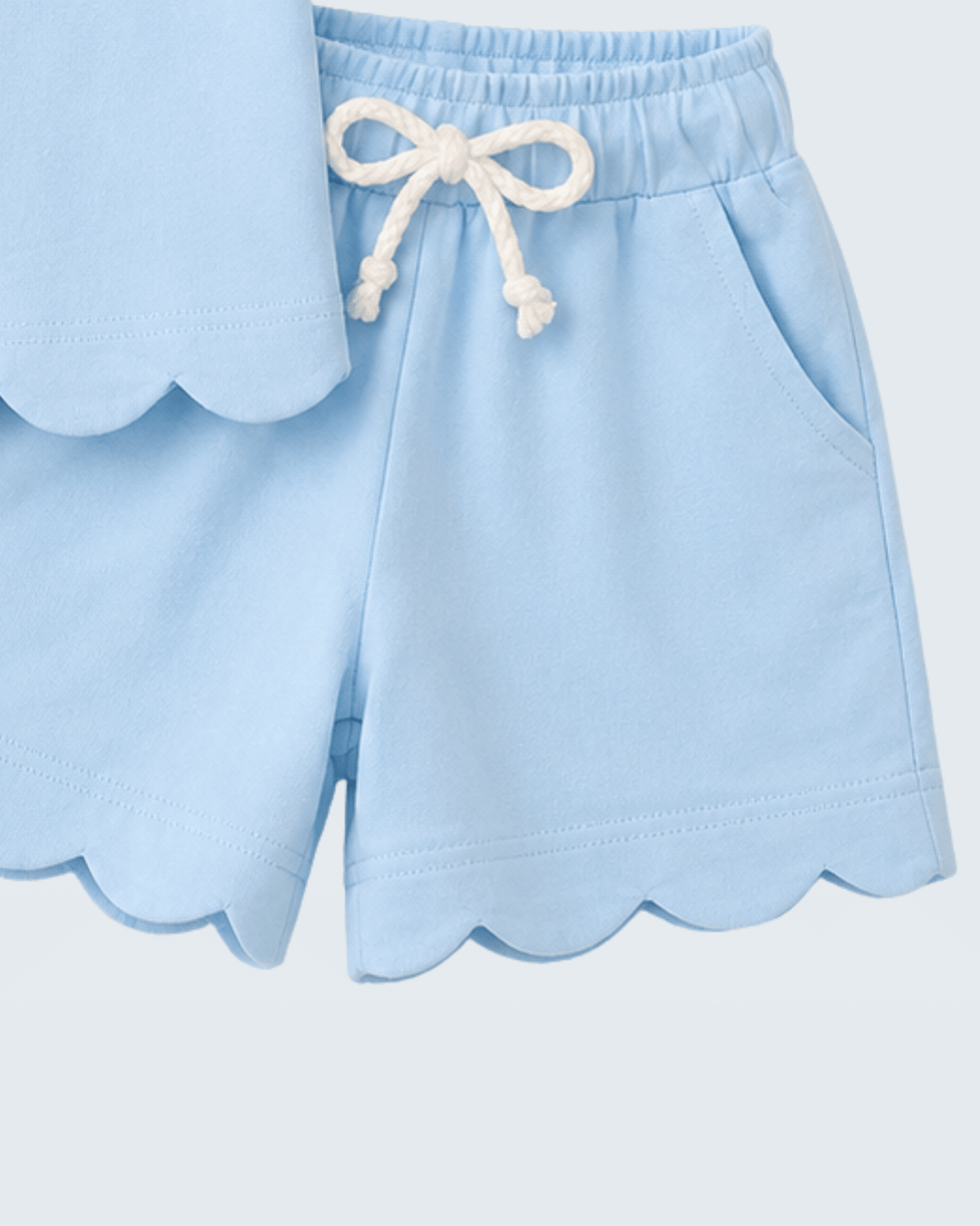 Light blue shorts with scalloped edges and a white drawstring on a light gray background