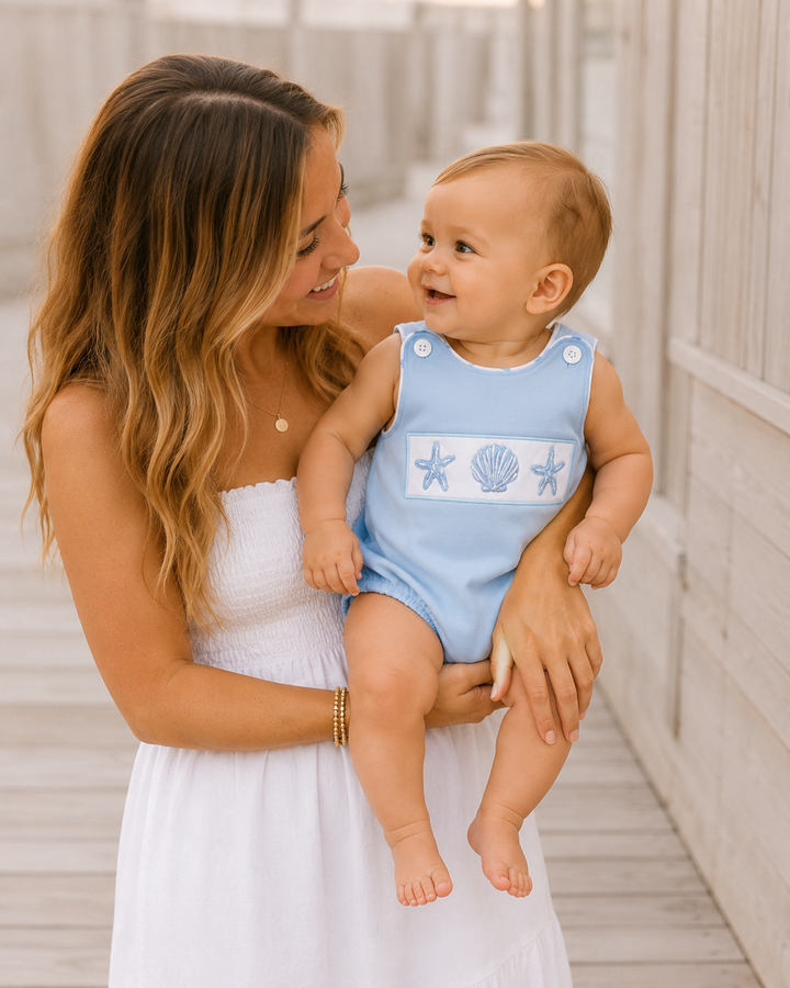 Woman holding a baby wearing a blue swimsuit with sea-themed design.