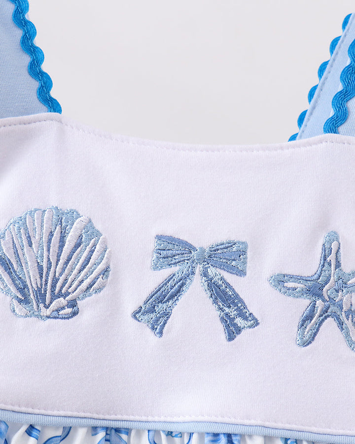 White dress with blue shell, bow, and starfish patterns on a white background