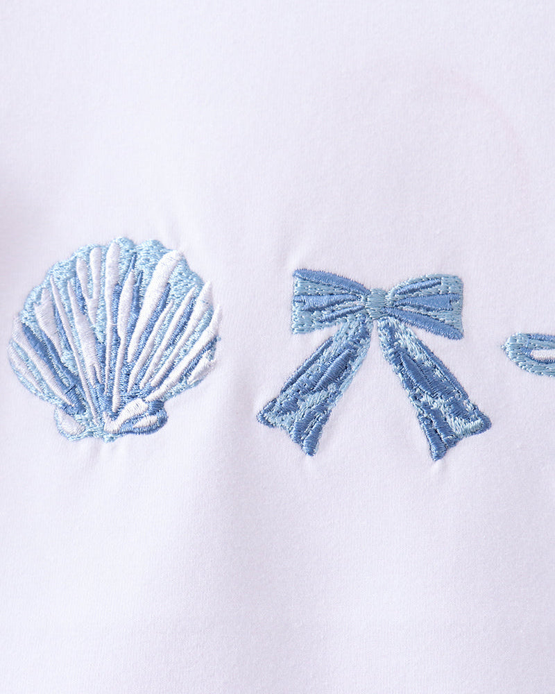 White shirt with blue embroidered shell and bow design on a white background