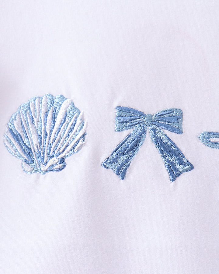 White shirt with blue embroidered shell and bow design on a white background